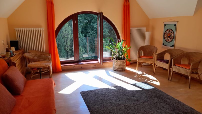 Heller Raum mit runden Fenstern, orangefarbenen Vorhängen und gemütlichen Sitzgelegenheiten.